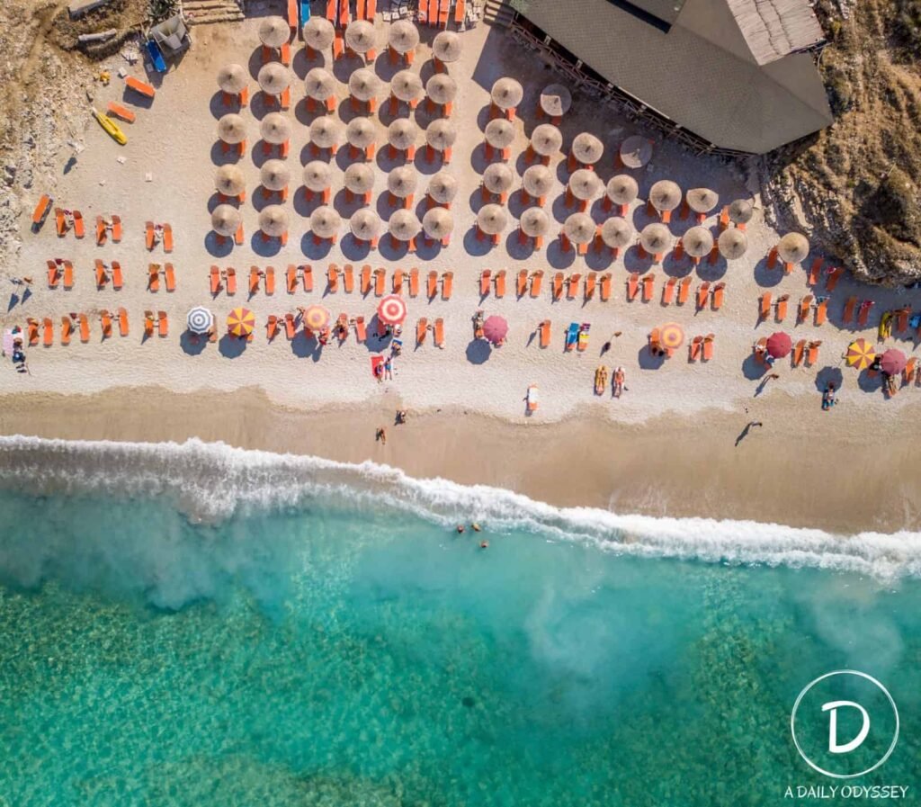 Mirror Beach in Saranda, Albania, showcasing the crystal-clear turquoise waters by aerial views and people in sunbeds