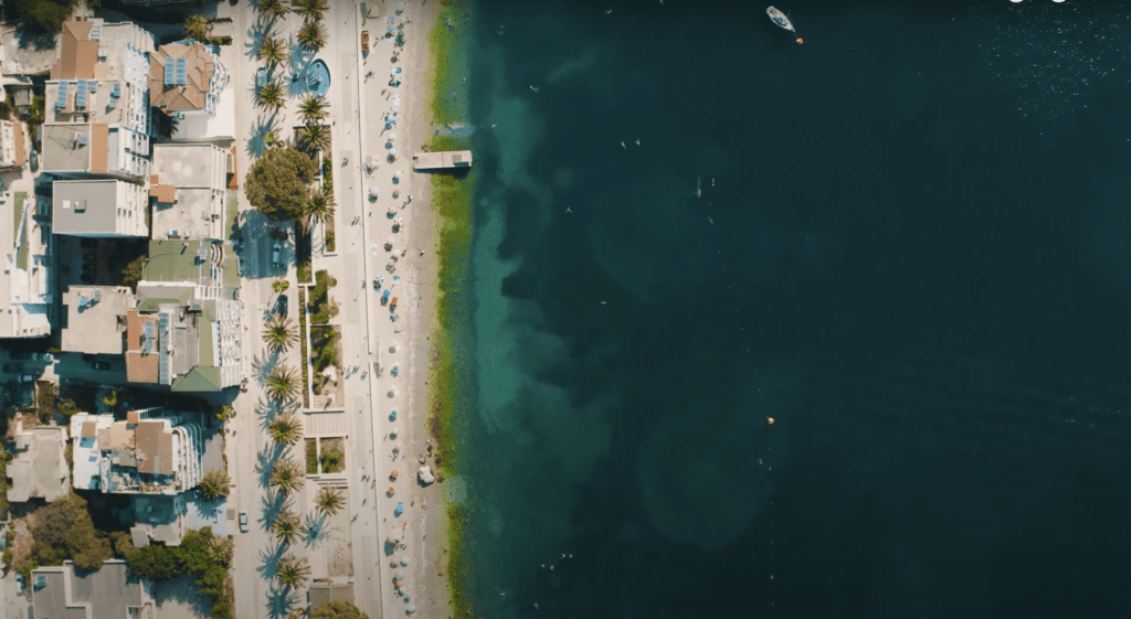 Bird's eye view of Saranda's picturesque waterfront promenade,  with a variety of restaurants, cafes, shops, and palm trees