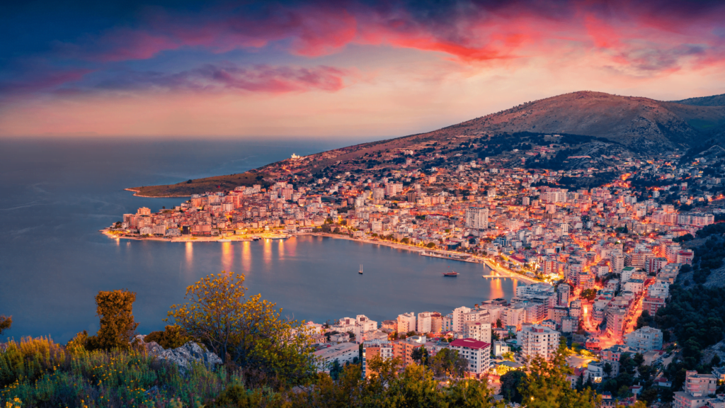 Sunset panorama over Saranda, capturing the bay, harbor, cityscape, promenade, architectural highlights, and the shimmering Ionian Sea