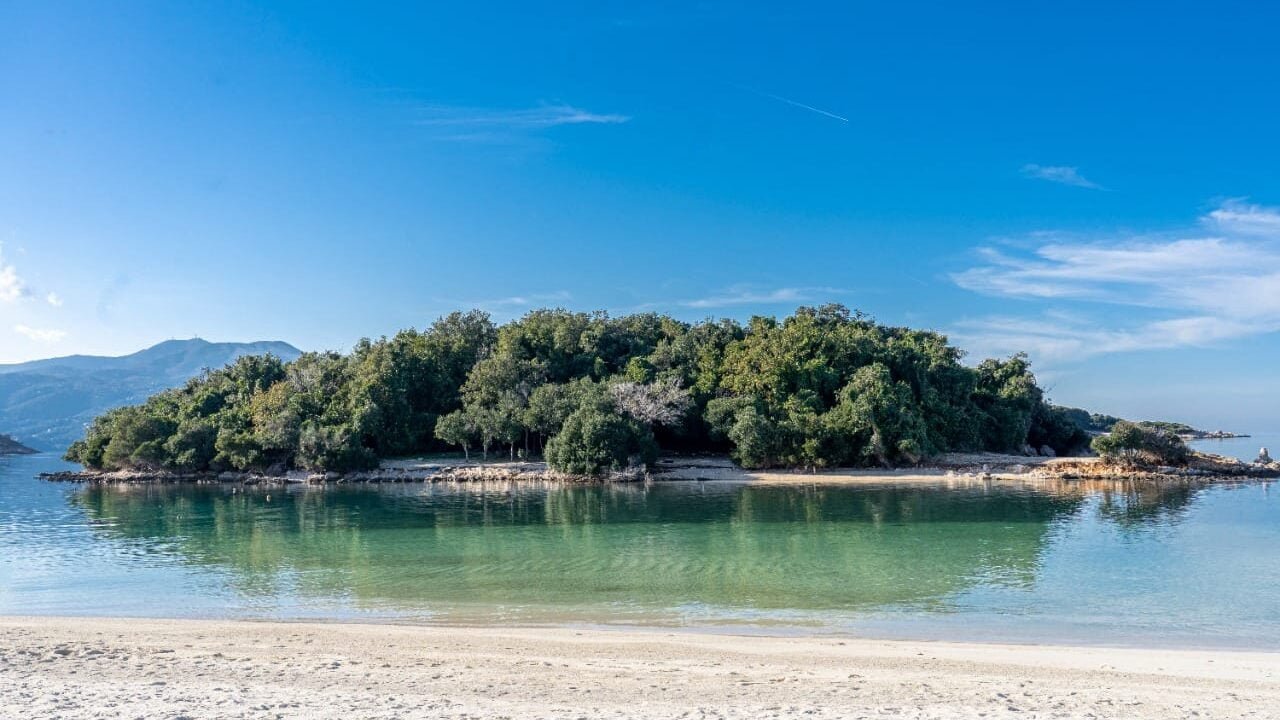 White sandy beach view in Ksamil, Albania, spotlighting one of its verdant islands amidst crystal-clear waters