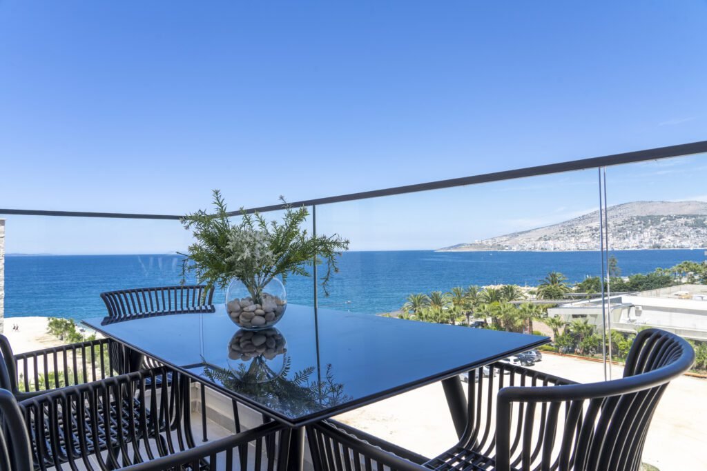 views of saranda, albania city from a penthouse balcony with high railings and black table on the waterfront above a sandy beach