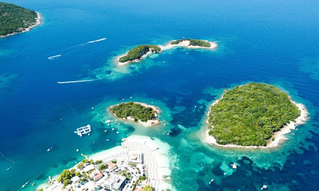 ksamil albania drone view of the 4 islands in the ionian sea waters , the city center with white sandy beaches with boats and people