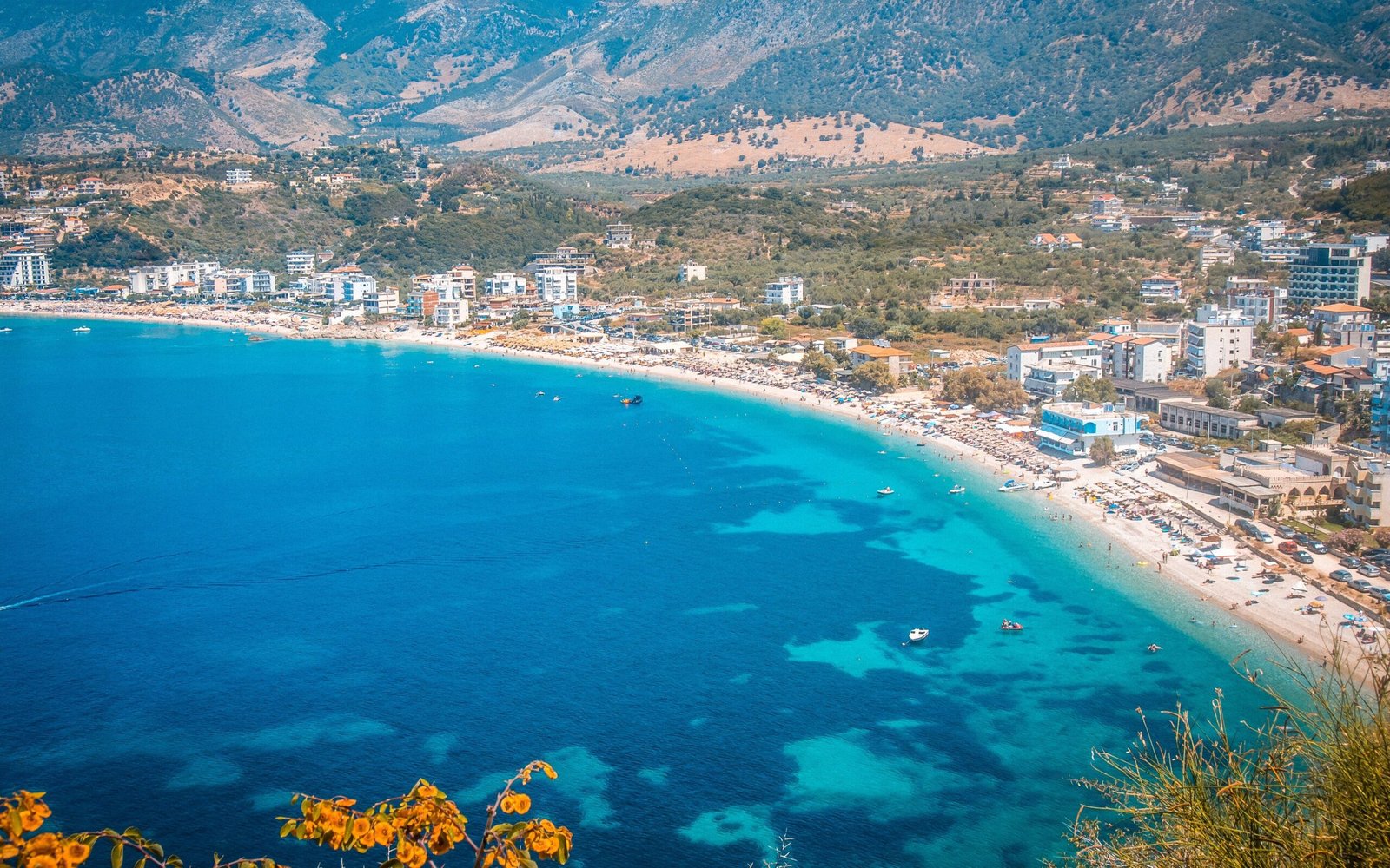 himare, Aerial drone view capturing the Ionian sea blue waters, the city's greenery, urban architecture, and surrounding mountains